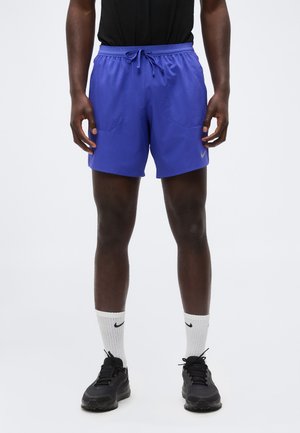 Mand iført lilla atletikshorts, hvide Nike crew-sokker og sorte løbesko, stående med hænder afslappet ned langs siderne.