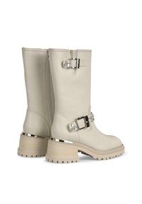 Botas de cuero beige hasta la rodilla con herrajes plateados, hebillas y acentos de tachuelas; suela texturizada con un grueso tacón cuadrado.