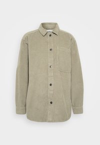 Chemise en velours côtelé vert olive avec un devant à boutons, un col pointu et une poche poitrine. Présente une texture en côtes verticales et des boutons noirs.