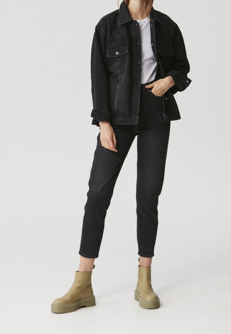 Black denim jacket over a white shirt, paired with black jeans and beige ankle boots. Features include a buttoned front and two chest pockets.