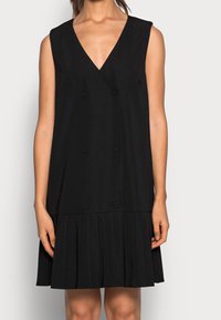 Abito nero senza maniche con scollatura a V, dettaglio di bottoni doppi e gonna plissettata. Tessuto morbido, lunghezza al ginocchio, stile minimale.