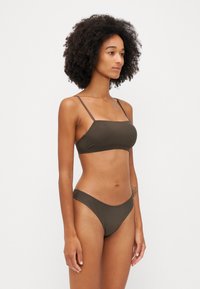 Brunt bikini-set med en bandeau-top med tynne stropper og matchende lavt skjørt nederst, med en jevn og elastisk tekstur.