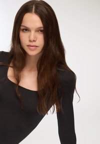 Czarna bluzka z długim rękawem i okrągłym dekoltem; gładka tekstura; noszona przez modelkę z długimi, ciemnymi włosami, na jednolitym tle.