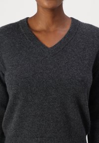 Maglione grigio scuro a collo a V realizzato in morbido tessuto a maglia con una texture liscia. Presenta un design aderente e un orlo a coste.