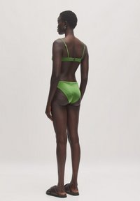 Groene bikini met verstelbare bandjes en een haaksluiting. Gladde stof met minimale bedekking aan de onderkant. Eenvoudig ontwerp zonder patronen.