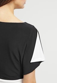 Svart och vit topp med lös passform, bred halsringning och kontrasterande korta ärmar. Slät tyg med mjuk textur.