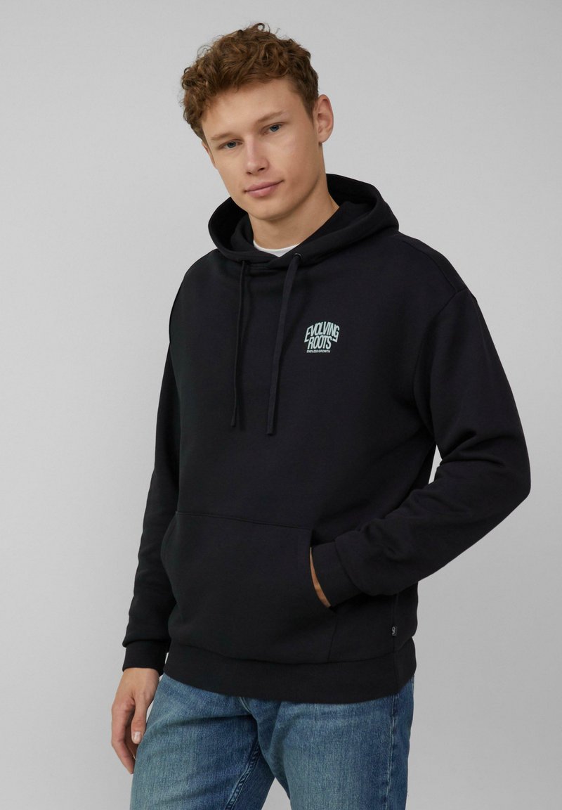 Zwarte hoodie van een katoenmix, met een kangoeroezak, trekkoordkap en een klein turkoois logo op de borst. Draagt met blauwe jeans.