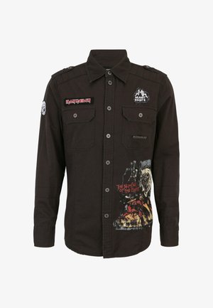 Juodas ilgomis rankovėmis marškinėliai su užsegimu priekyje, su lopais ir meno kūriniais. Išskirtinės detalės apima grafišką atspaudą "Baisumo skaičius".