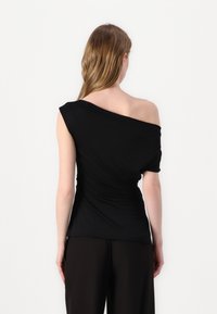 Czarny top na jedno ramię z marszczeniami, dopasowany fason i miękka tekstura. Noszony z czarnymi spodniami o szerokich nogawkach, prezentując minimalistyczną estetykę.