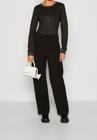 Czarna bluzka z długim rękawem o teksturowanym wzorze; czarne spodnie cargo z wysokim stanem; biała torebka o sztywnym kształcie; czarne masywne botki.