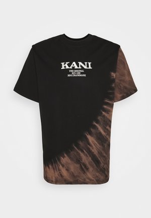 Mand iført en sort og brun tie-dye T-shirt med hvid tekst, marineblå cargoshorts, hvide sokker, sorte sneakers og sølvkæde halskæde.
