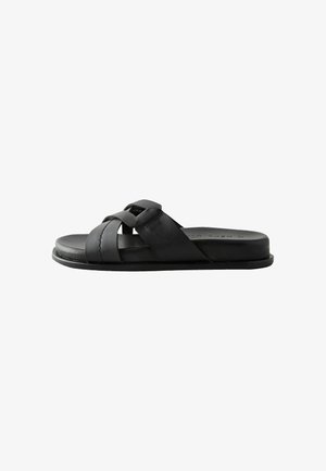 Sort læderslide-sandal med krydsede remme og flad sål, vist fra siden på en hvid baggrund.