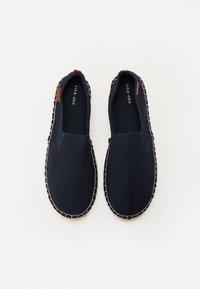Baskets navy à enfiler avec tige en maille, accent en cuir marron et couture beige contrastante sur la semelle. Design léger et respirant.