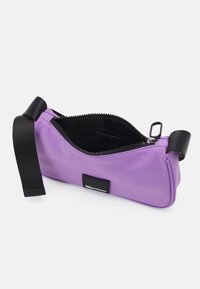 Bolso bandolera rectangular púrpura con correa negra ajustable, cremallera abierta que muestra el interior negro y una pequeña etiqueta externa.