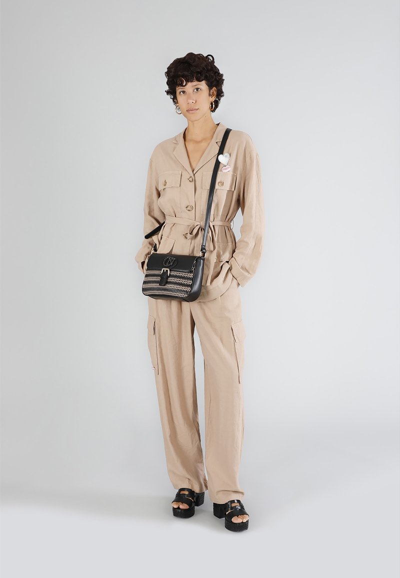 Beige, långärmad jumpsuit med knyt i midjan, knappstängning och fickor; matchad med en svart axelväska med flätad detalj och metalliska accenter.