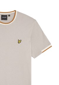 T-shirt grigio chiaro a maniche corte con scollo rotondo, caratterizzato da un logo di uccello ricamato giallo e nero sul lato sinistro del petto e accenti in contrasto sul collo e sulle maniche.