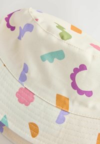 Bucket-hatt av krämfärgad tyg med färgglada abstrakta former i lila, grönt, rosa, blått, orange och gult. Sömmar synliga.