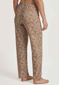 Bloemen pyjamabroek met een elastische tailleband, met een roze, oranje en groene print op een lichte beige achtergrond. Losvallend ontwerp.