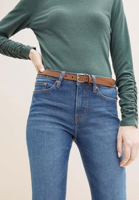 Camisa verde de manga larga combinada con jeans de tiro alto azules, que cuenta con un cinturón de cuero marrón asegurado con una hebilla de plata.