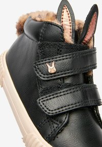 Svarta sneakers för barn med fuskpälsfoder, kaninöronaccenter, två kardborreband och en liten metallkaninpin på bandet.