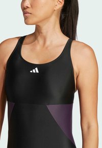 Schwarzer Schwimmanzug mit gerundetem Ausschnitt, dünnen Trägern und einem kontrastierenden lila Einsatz an der Taille; glattes, dehnbares Material.