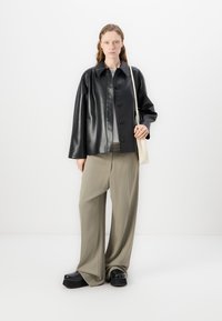 Jachetă din piele neagră cu închidere cu buton, croi supradimensionat; bluză gri dedesubt. Pantaloni bej deschis, lungi, cu croi larg, pantofi negri cu platformă și o geantă.