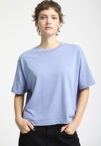 T-shirt in cotone azzurro chiaro con collo rotondo, maniche corte e vestibilità comoda. Presenta un logo minimalista sul petto.