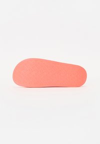 Rosa gummiskosula med texturerat mönster där ordet "GUESS" upprepas över hela ytan. Slät, rund kant med platt botten.