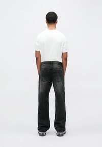 Črne kavbojke iz jeansa z ohlapnim krojem in vidnim šivom, kombinirane s preprosto belo majico. Preprost dizajn z nevtralno barvno paleto.