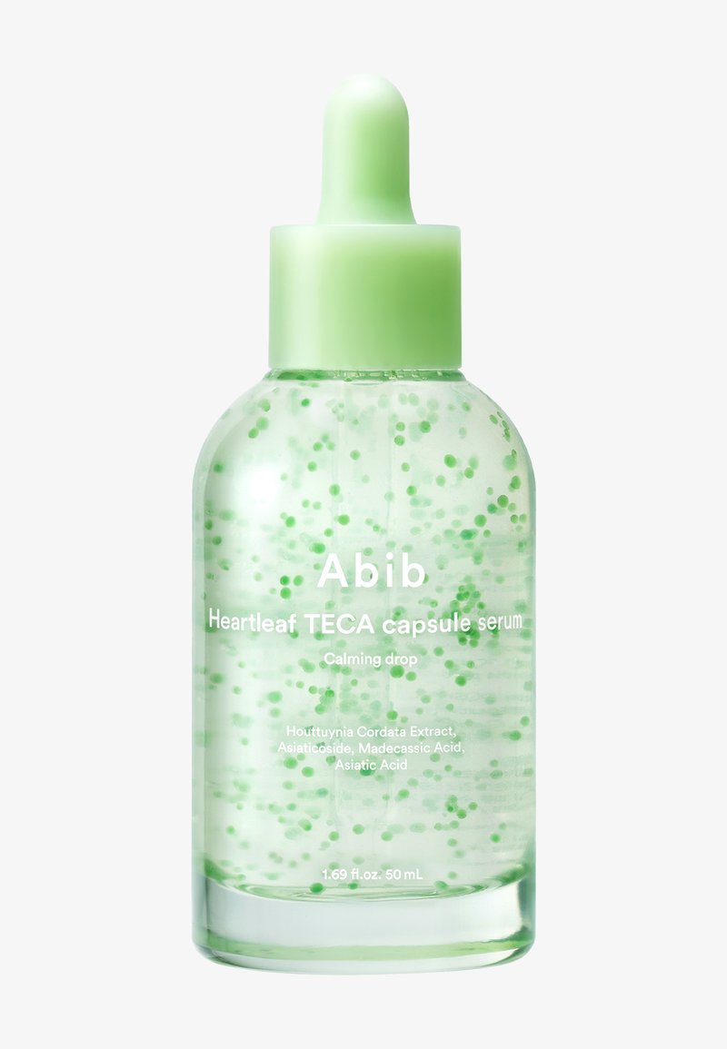 Heldere glazen druppelfles met een groen gesloten dop, gevuld met transparante serum met zwevende groene capsules, gelabeled "Abib Heartleaf TECA capsule serum."