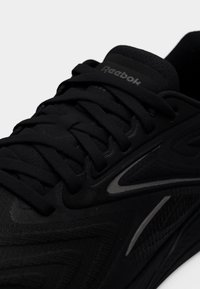 Κοντινό πλάνο μαύρου αθλητικού παπουτσιού Reebok με υφασμάτινη υφή, χοντρές κορδόνια και διακριτική αντανακλαστική σήμανση στη πλευρά και στη γλώσσα.