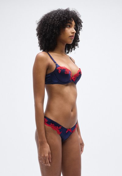 Σετ εσωρουχών σε ναυτικό μπλε χρώμα με σουτιέν με μπανέλα και κόκκινη δαντέλα, συνοδευόμενο από μπικίνι εσώρουχο με δαντέλα και λεπτομέρειες από κορδέλα.