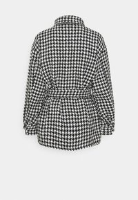 Cappotto a fantasia pied-de-poule in bianco e nero; presenta una vita con cintura, colletto e maniche lunghe; tessuto strutturato con una vestibilità definita.