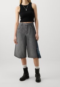 Top corto negro, culottes de mezclilla gris, de largo hasta la mitad de la pantorrilla, de talle alto, con dos bolsillos frontales, acompañado de botas negras hasta el tobillo y calcetines blancos.