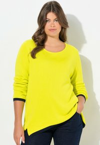 Maglione giallo brillante con scollo rotondo, maniche lunghe e orlo asimmetrico. I polsini blu scuro accentuano le maniche. Texture morbida.