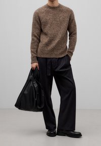 Brązowy, teksturowany sweter z dzianiny z okrągłym dekoltem, zestawiony z luźnymi czarnymi spodniami i dużą czarną skórzaną torbą. Stylizację dopełniają czarne buty.