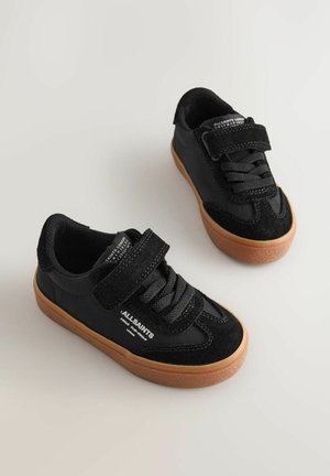 Mustad võimlemisjalatsid, mis on valmistatud võrgust ja seemisnahast ning millel on kummist tallad. Disainis on kinnitusnöörid, Velcro-rihm ja brändi märk külje peal.