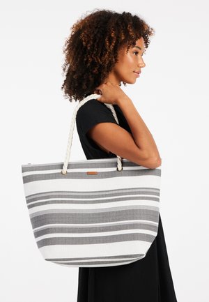 Sac fourre-tout rayé en toile, avec des rayures grises et blanches, une poignée en corde et une petite étiquette en cuir marron à l'avant.