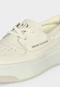 Κοντινή λήψη ενός λευκού sneaker Armani Exchange με κορδόνια, διάτρητη μύτη και σήμανση στο πλάι και στη γλώσσα.