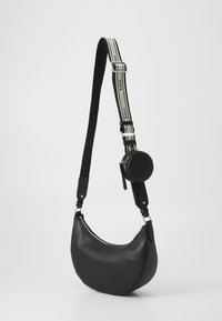 Bolso de hombro de cuero negro con forma curva, que presenta una correa en contraste con la marca "BOSS" y un bolso redondo extraíble.