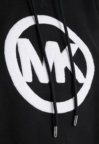 Felpa nera con cappuccio caratterizzata da un grande logo in spugna bianca con "MK" all'interno di un cerchio. Lacci neri con estremità in metallo. Texture del tessuto morbida.