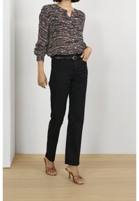 Camicia nera con bottoni e un motivo astratto multicolore, abbinata a pantaloni neri a gamba dritta e tacchi a strappo marroni.