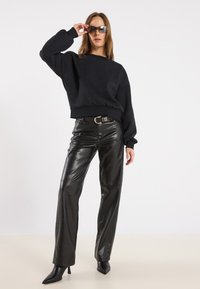 Felpa nera con maniche larghe, abbinata a pantaloni in pelle nera lucida a vita alta. Indossa tacchi a spillo neri e occhiali da sole scuri.