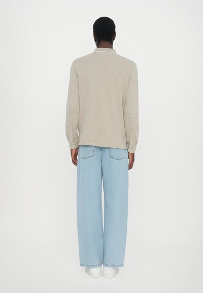 Camisa bege de mangas longas com punhos abotoados, combinada com jeans de perna larga azul claro. O conjunto apresenta um ajuste descontraído e uma textura suave.