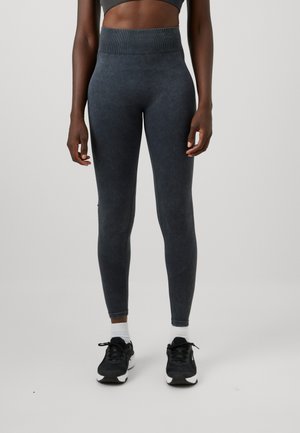 Person wearing high-waisted dark gray leggings, white socks, and black athletic shoes, standing against a plain light gray background.