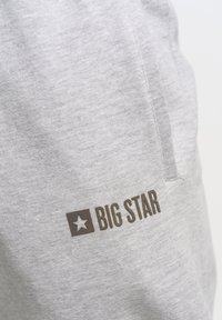 Grijze katoenen joggers met een zijzak en een donkerbruin "BIG STAR" logo met een stergrafiek op de linker bovenbeen. Zachte textuur.