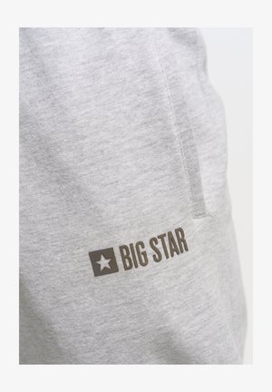Joggers de algodón gris con un bolsillo lateral y un logo "BIG STAR" en marrón oscuro con un gráfico de estrella en el muslo izquierdo. Textura suave.
