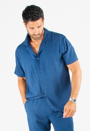 Chemise à manches courtes, en bleu marine uni, fabriquée en matériau léger. Elle présente une coupe décontractée, un col plat et deux poches avant.
