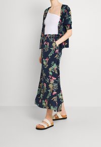 Floral two-piece set with a navy background; includes a fitted white tank and a flowy skirt with vibrant flowers and leafy patterns. Worn with light sandals.