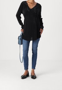 Musta pitkähihais-toppi, jossa on ribbitekstuuri, V-mallinen kaula-aukko ja rypytys yksityiskohtana, yhdistettynä sinisiin farkkuihin ja mustiin niittikengiin.